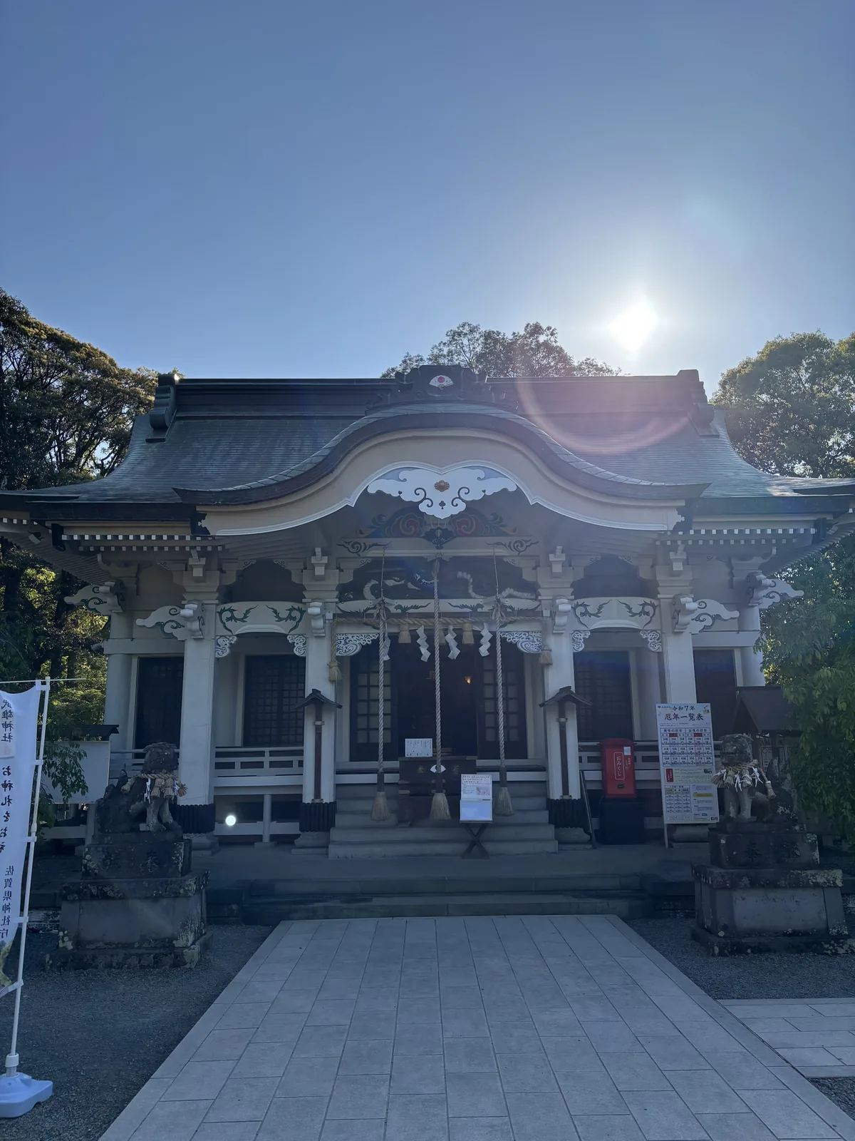 武雄神社的拜殿正面，白牆青綠色屋頂，正面有唐破風，逆光下太陽在屋脊上方