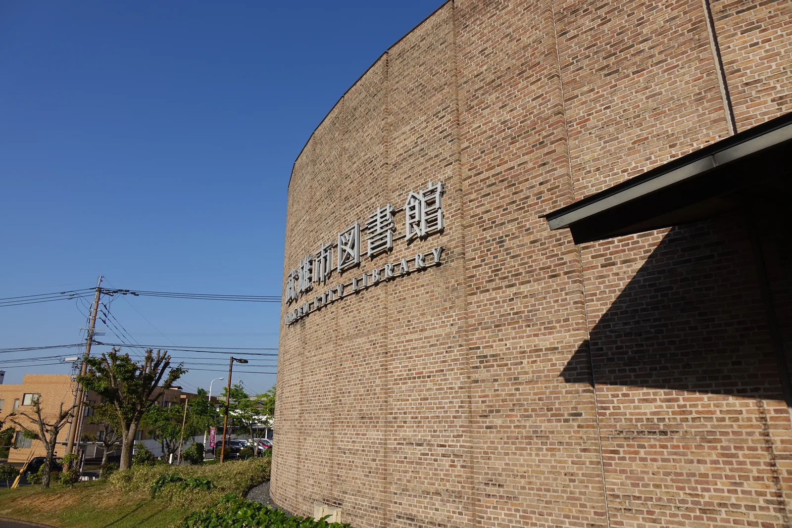 圖書館的弧形磚牆，牆上有金屬字「武雄市図書館 TAKEO CITY LIBRARY」