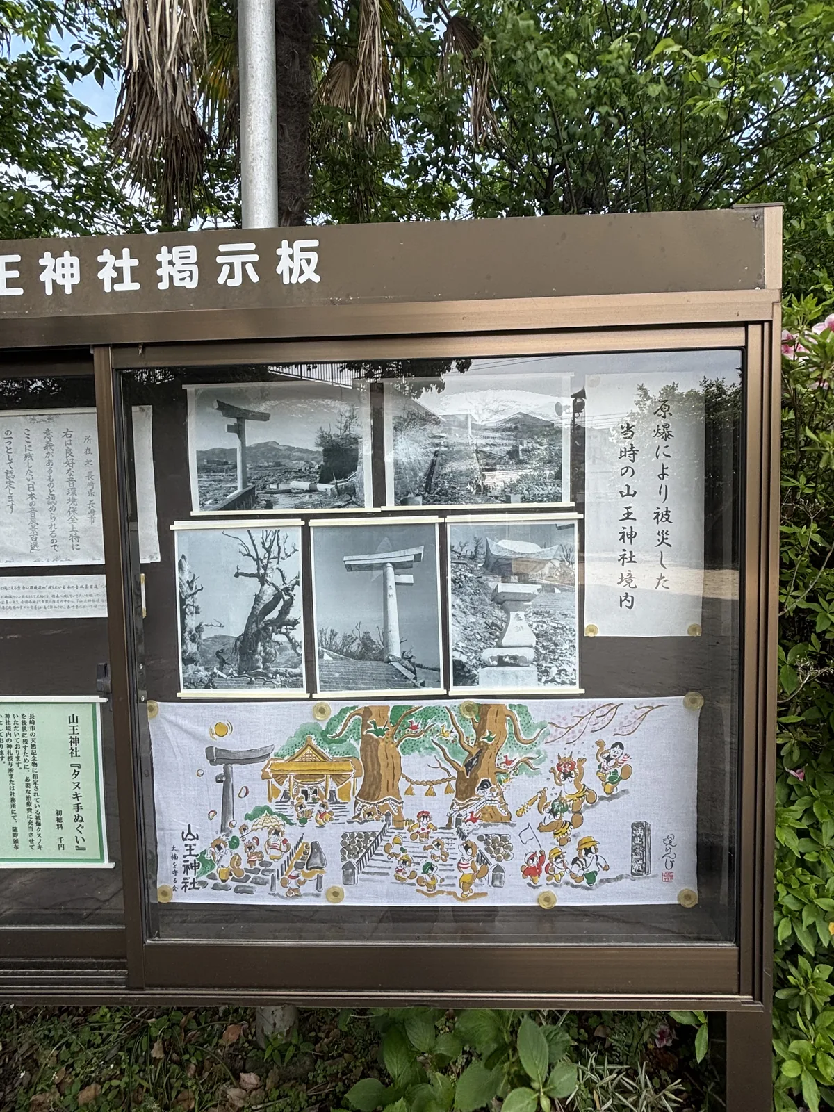 神社掲示板，上半是原爆當時境內的黑白照片，下半掛著印滿狸圖案的手巾