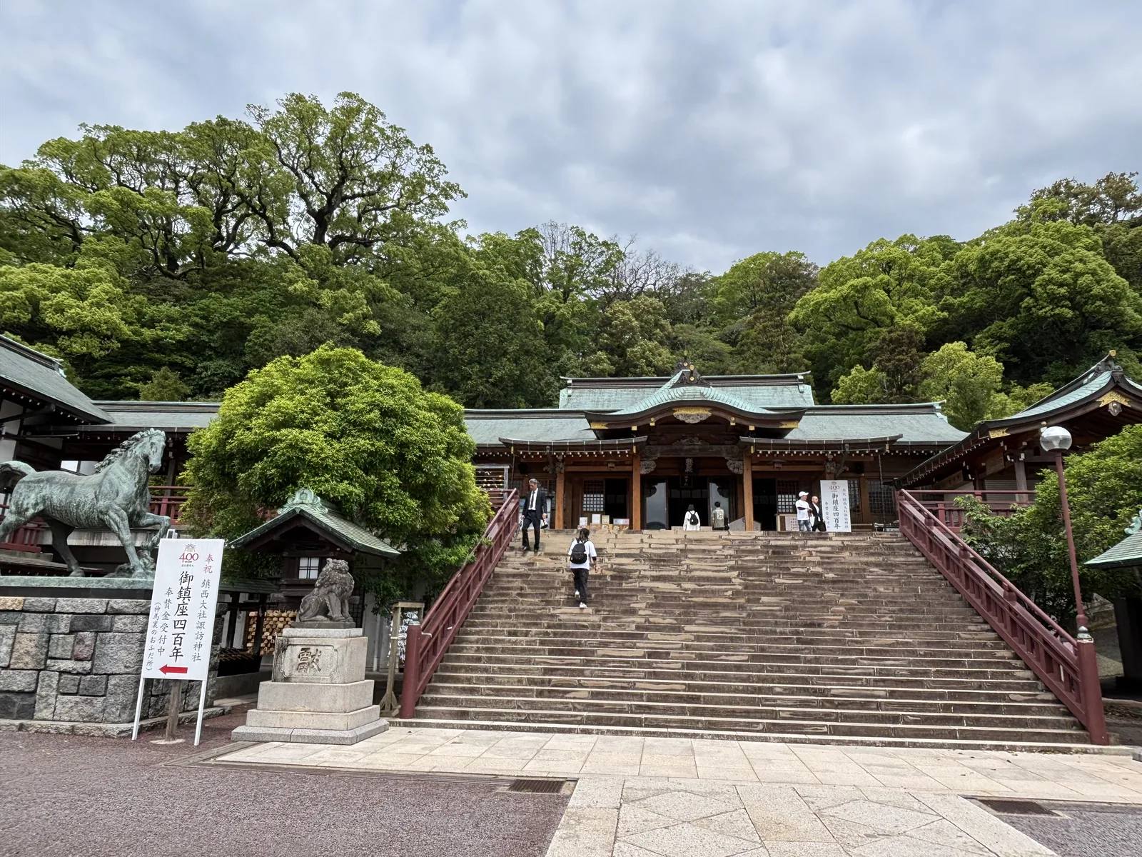 諏訪神社的拜殿前廣場，左側是青銅神馬像，中央立著御鎮座四百年的白幟，右側石階通往上方的拜殿