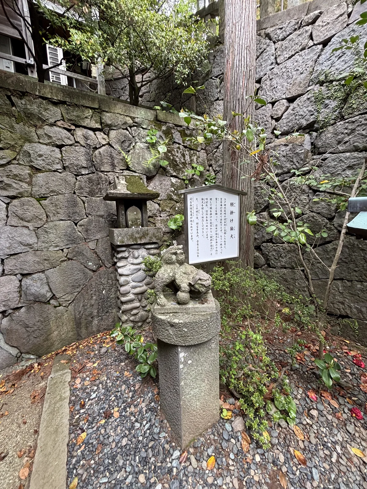 諏訪神社境內的願掛け狛犬與說明板，狛犬立在石台上，後方是石垣與一座小祠