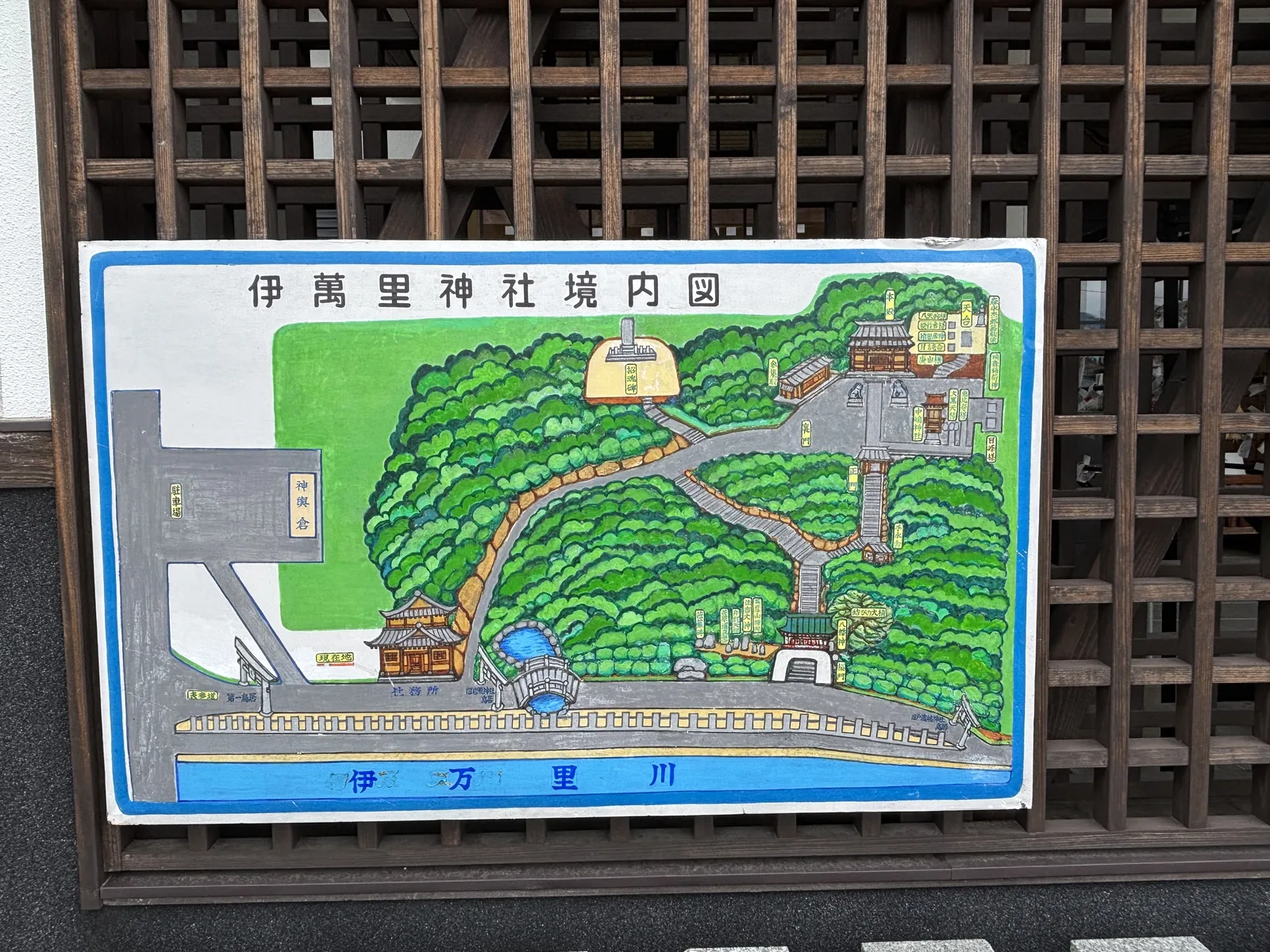 伊萬里神社的手繪境內圖看板，掛在木格柵牆上，畫著丘上的社殿群與丘下的社務所、伊万里川