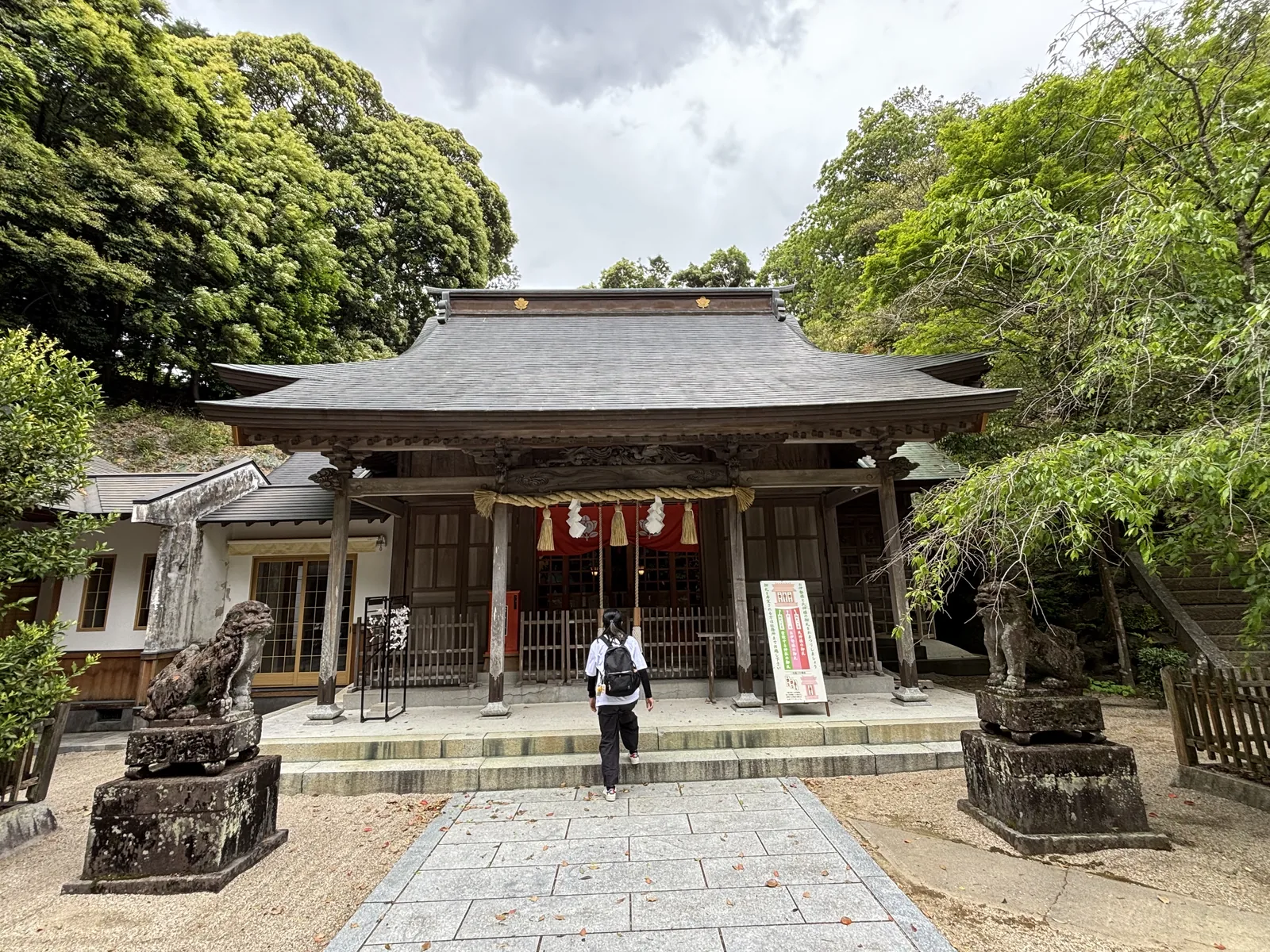 伊萬里神社的拜殿正面，入母屋造帶向拜，深褐色木構，注連繩下垂兩束稻藁，兩側高台座上各一狛犬