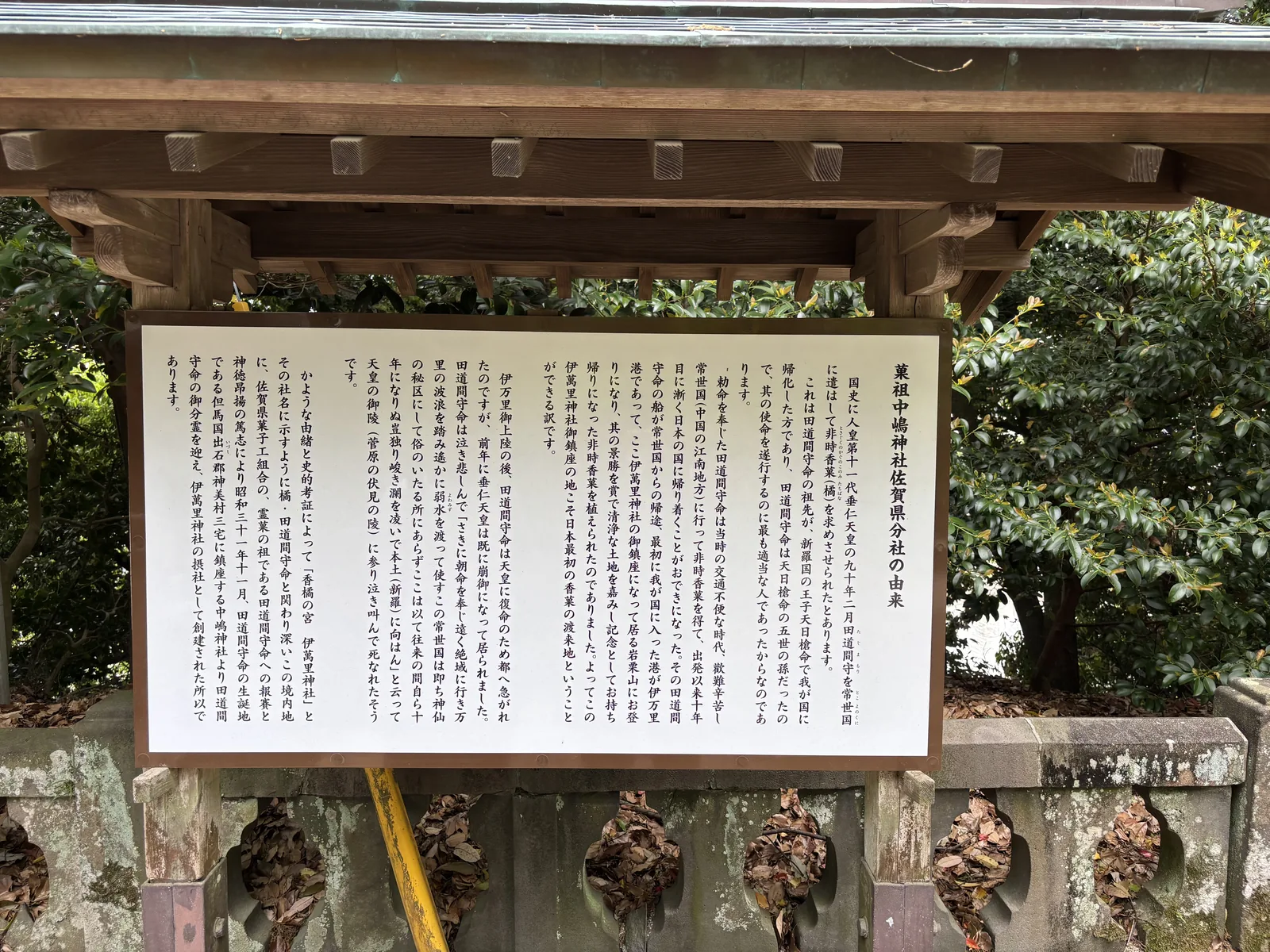 中嶋神社佐賀縣分社由來的說明看板，白底直排日文，掛在木造的簡易屋簷下