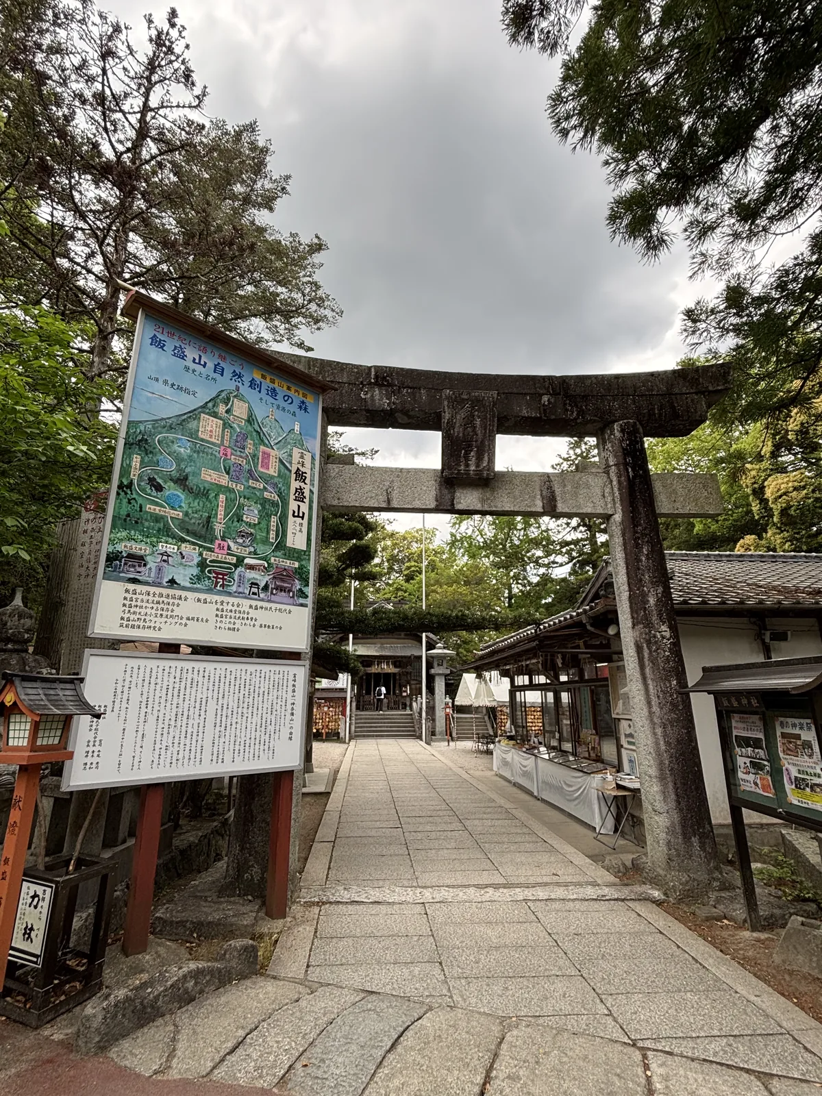 飯盛神社的二之鳥居與兩塊案內板，一塊是手繪的飯盛山鳥瞰圖，一塊是密排直書文字的由緣板