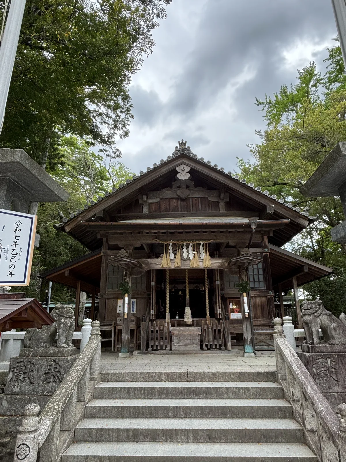 飯盛神社的拜殿正面，素木造，中央垂著粗注連繩與鈴繩，兩側石燈籠與狛犬，前方幾階石階