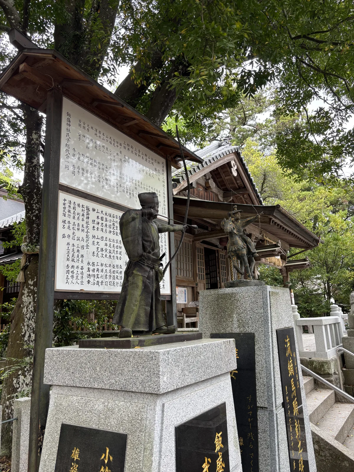 飯盛神社拜殿前的兩座銅像，左邊是站立拉弓的武者，右邊是騎馬拉弓的流鏑馬射手，旁邊立著流鏑馬顕彰之碑
