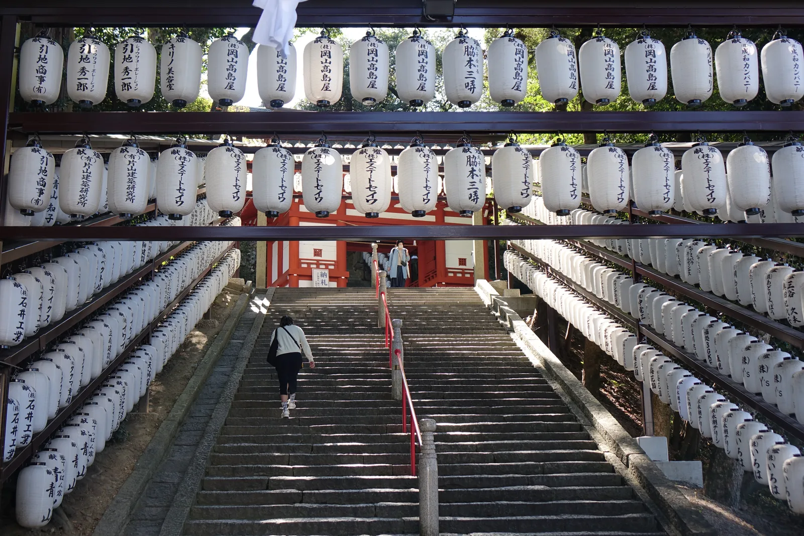 吉備津神社北參道的石階：兩側木架上一層層排滿白色紙燈籠，把石階夾成一條白色甬道，盡頭是朱塗的北隨神門