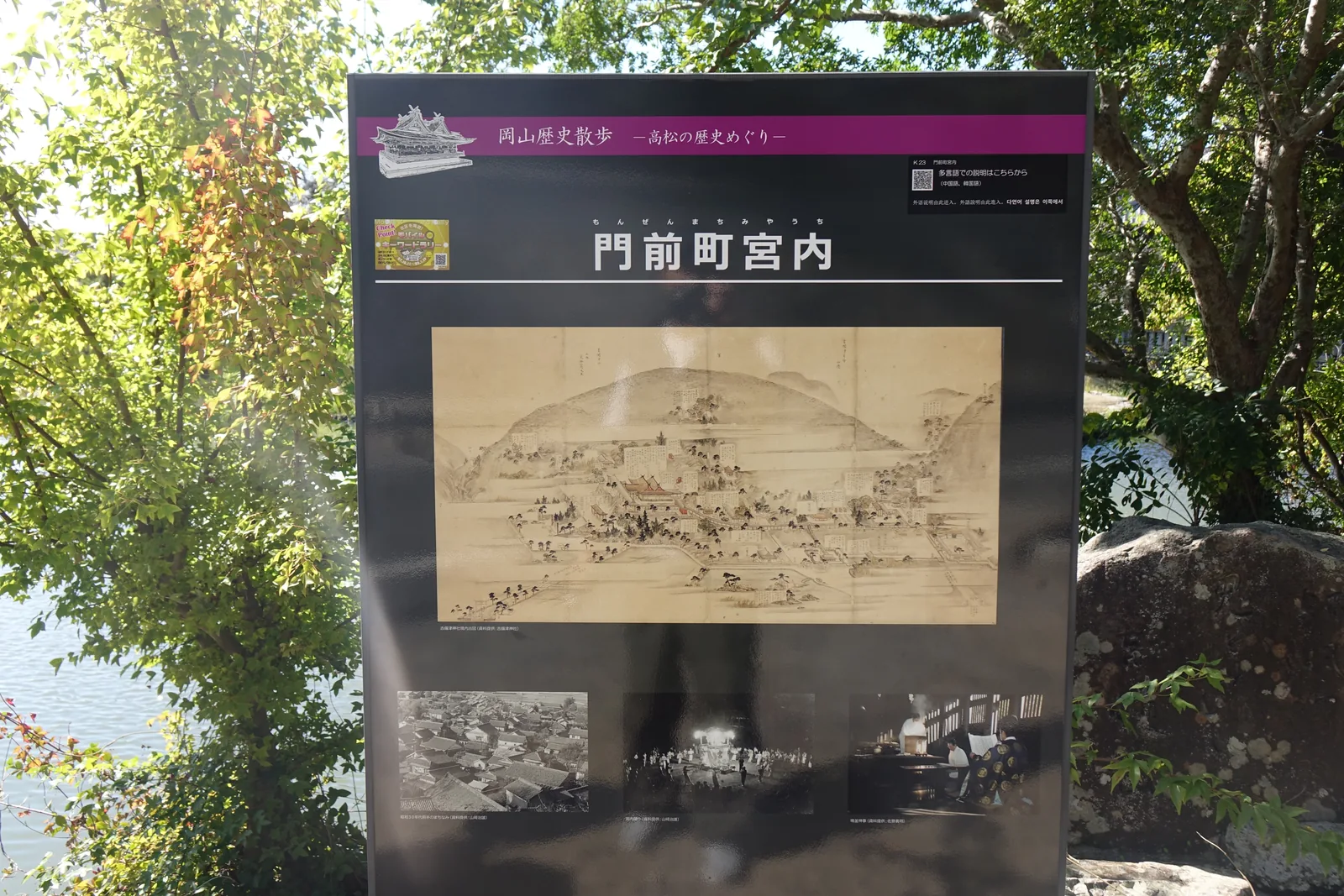 境內西側的岡山歷史散步「門前町宮內」說明板，主圖是吉備津神社境內古圖的複製，底下三張黑白照片分別是町並俯瞰、夜裡的祭典行列與御竈殿裡的鳴釜神事