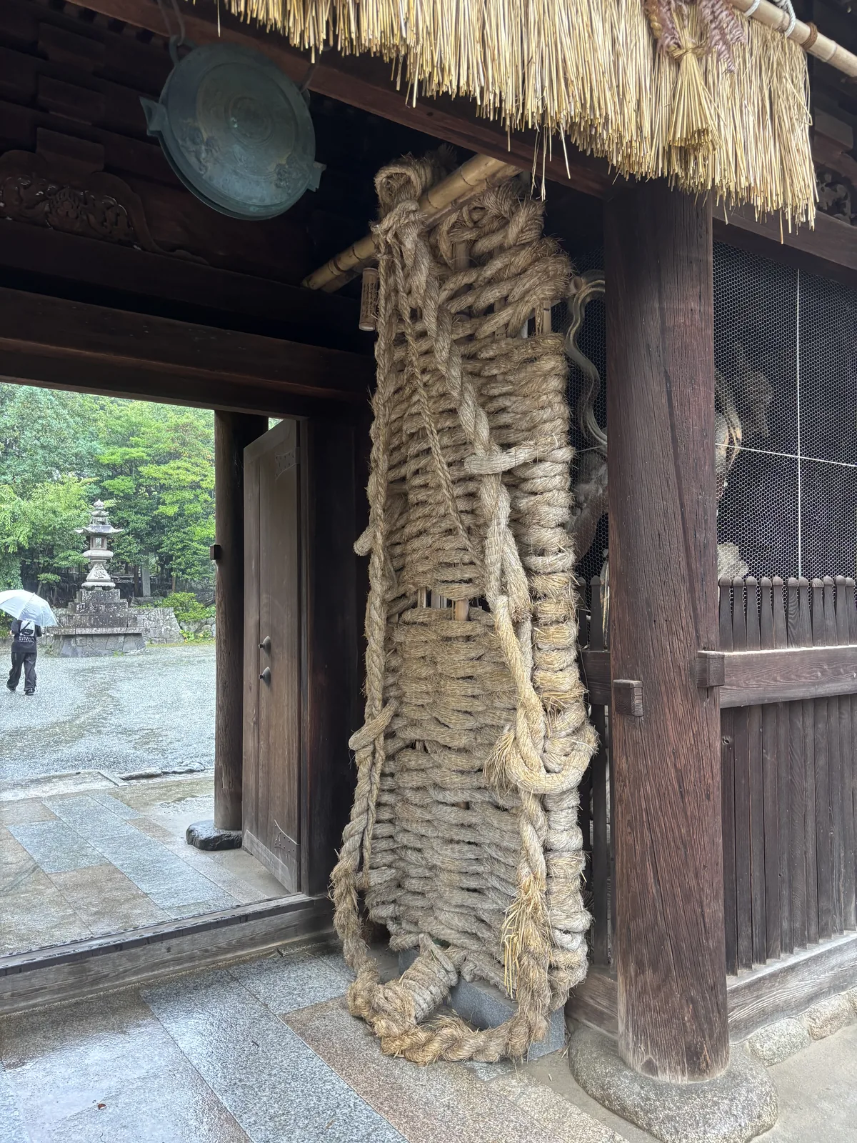 國寶二王門的內側。柱邊靠著一雙比人還高的大草鞋，草繩曬成灰白、一層層疊起來，上方垂著剛換過的新藁。右側格柵後面是金剛力士立像——門在一九五二年成為國寶，門裡的像到二〇二二年才被指定為重要文化財。