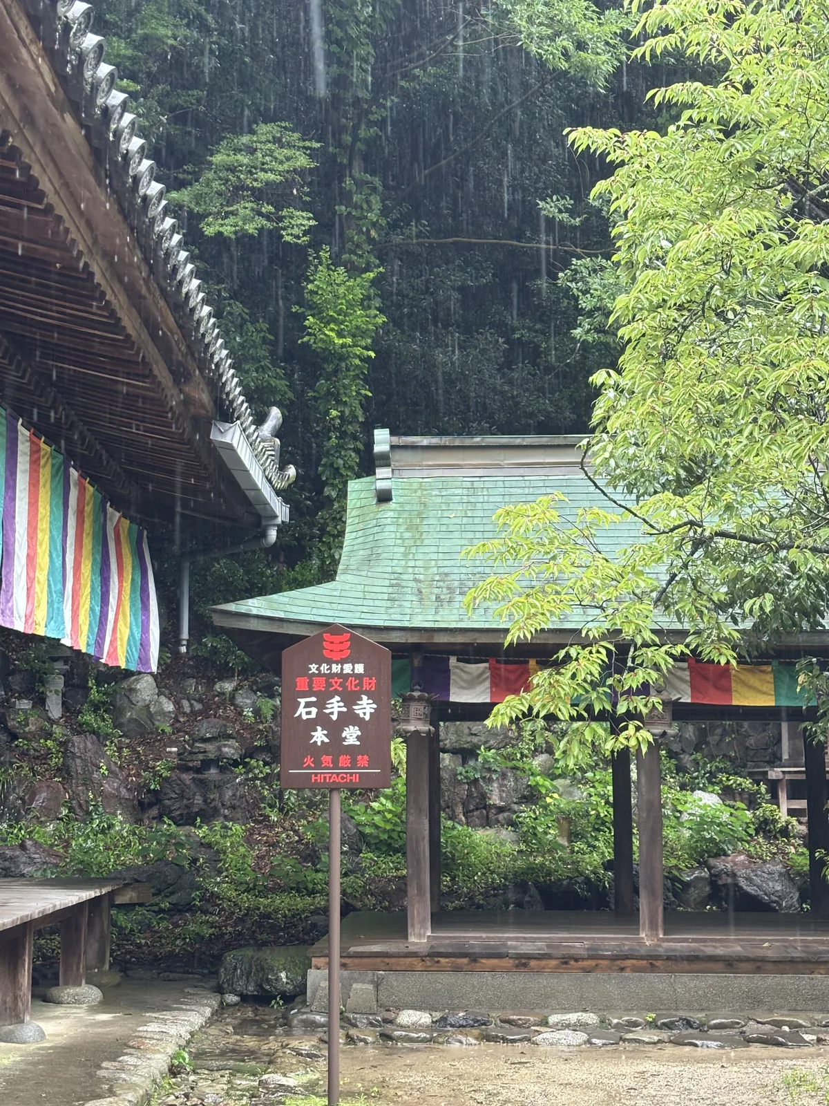 本堂前的紅底立牌，寫著「文化財愛護　重要文化財　石手寺本堂　火氣嚴禁」。後方是石垣與愛宕山的斜面，五色幕沿著簷下拉開。