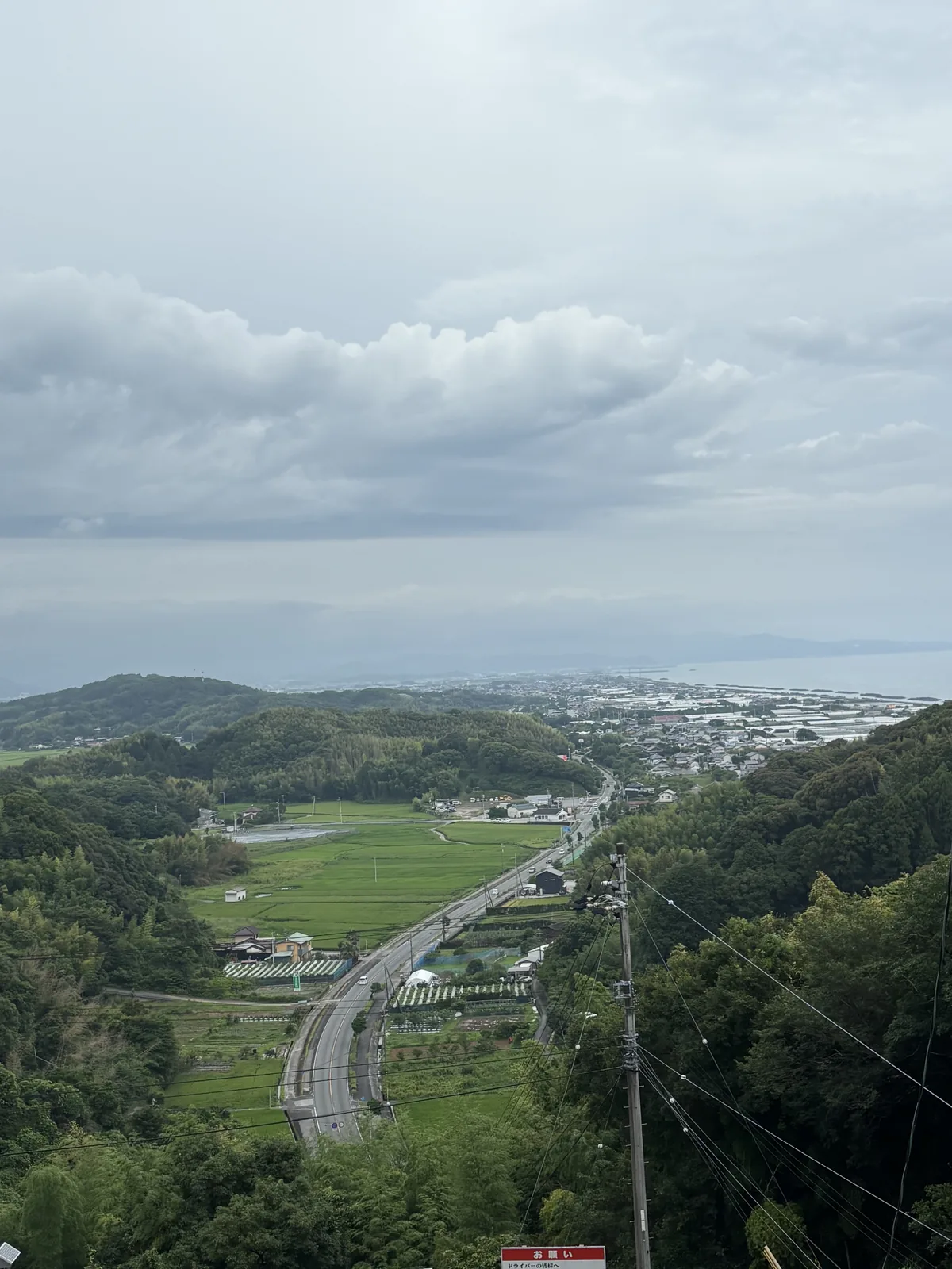 從山道上往北看下去，路彎下坡，前方是水田與集落，更遠是低矮的丘陵。