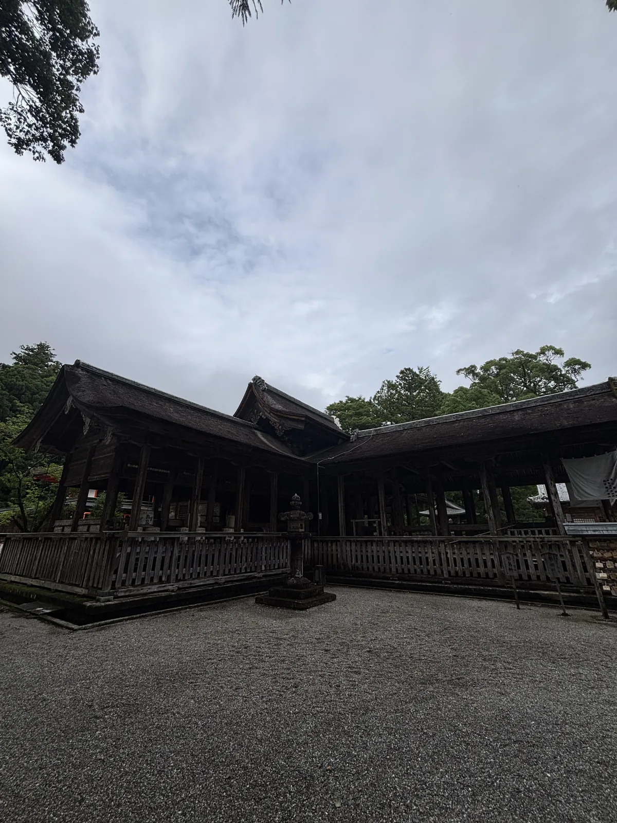 入蜻蛉的全景。左右兩道低矮的切妻翼廊向前伸出，在中央交會處抬高成重層的切妻屋頂。屋面是こけら葺，前方是碎石地。一張照片就把這個平面說完了。