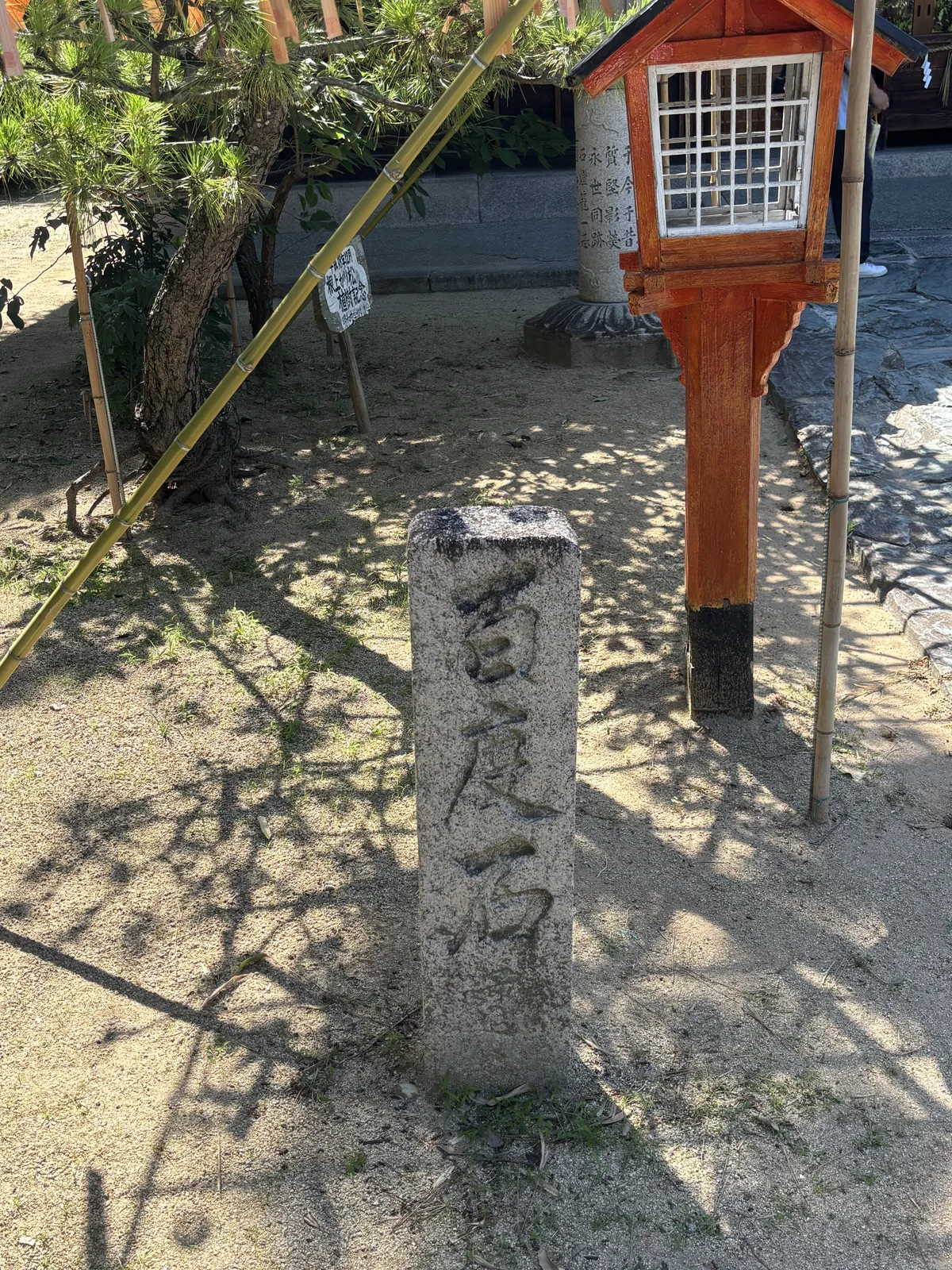 白沙地上一根方形石柱，正面刻「百度石」；旁邊是朱塗的木燈籠與竹製的低欄。