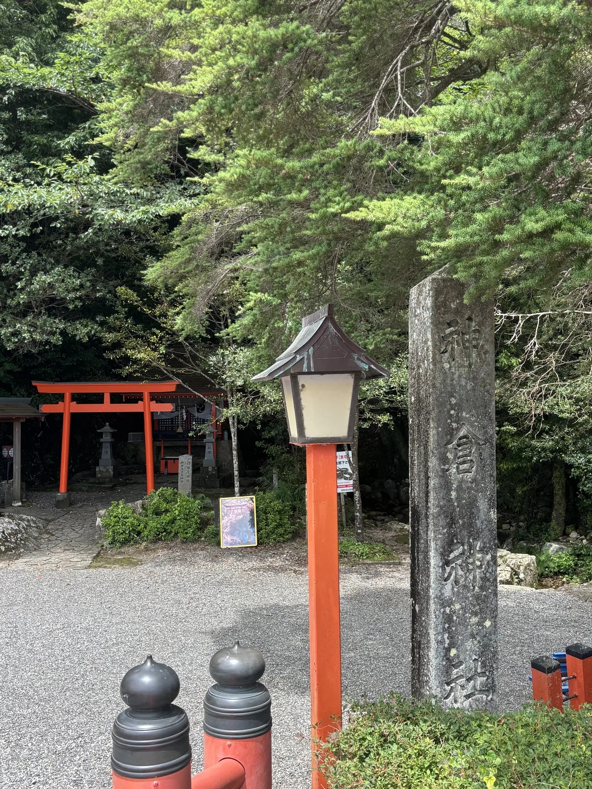 風化嚴重的石標直刻「神倉神社」，旁邊一支朱色燈柱。後方是一之鳥居、兩座石燈籠與社務所。這一段還是平的。左側草地上立著黃框的御燈祭照片看板。