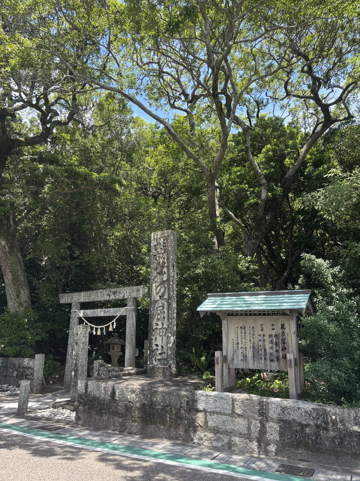 國道邊的石造社號標與木構說明板，後方是石鳥居。柏油路面的白線就在腳下——神社與七里御濱之間隔著國道四十二號。