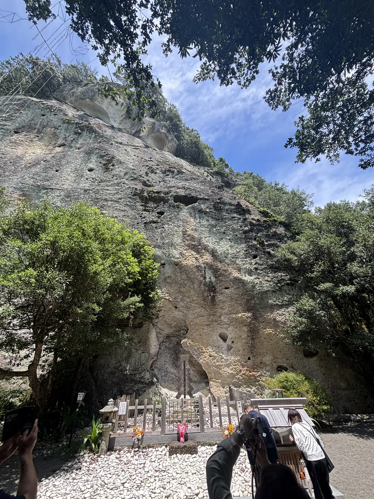 岩根的祭壇與白石鋪面，一圈木造玉垣高度只到膝蓋。人站在白石上抬頭，岩壁一路往上收，把天空切成一條窄的。