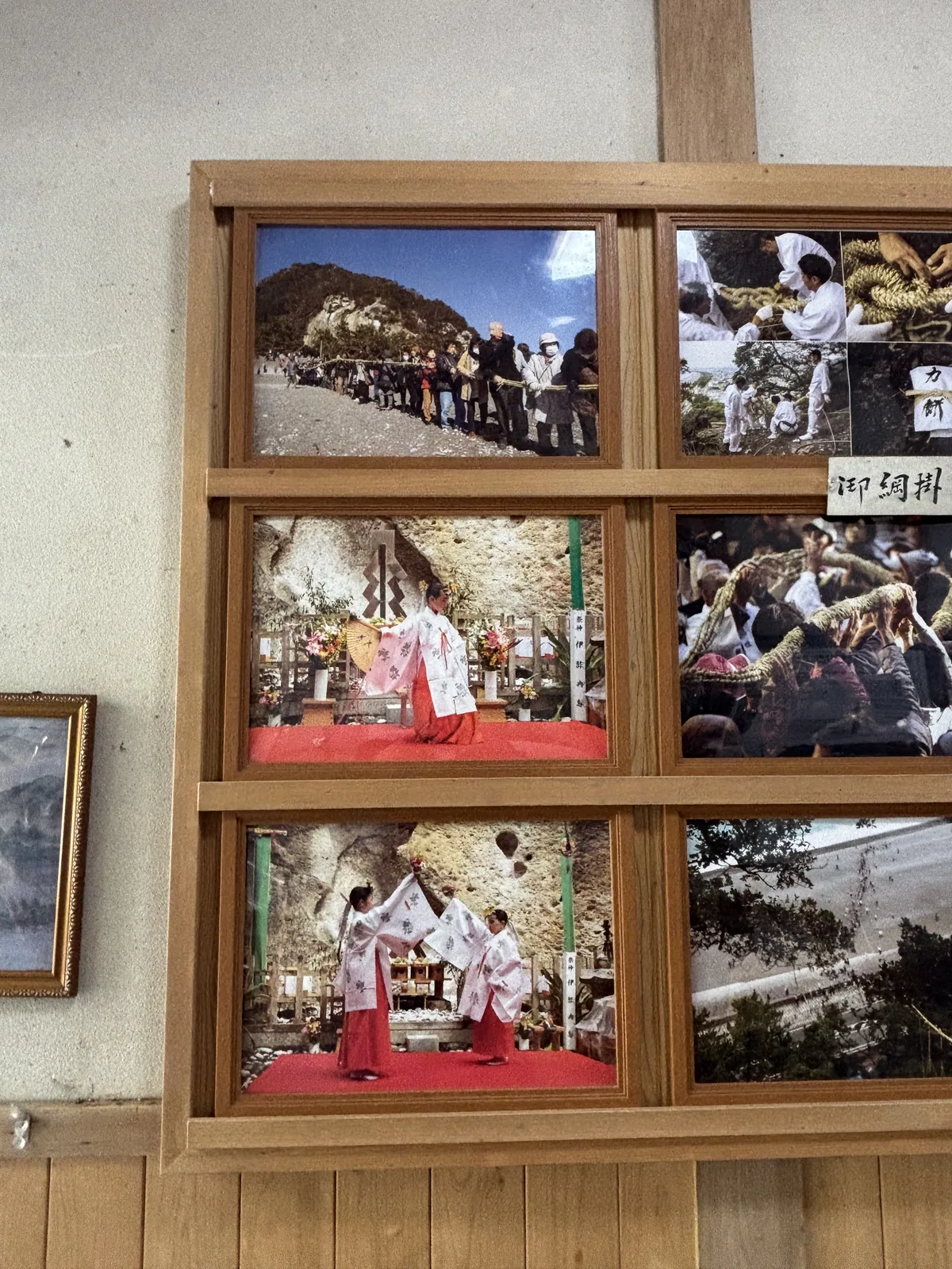展示室牆上的連續照片，標題「御綱掛け神事奉仕手順写真」。人群在七里御濱的礫灘上拉繩，紅毯鋪在拜所前由巫女起舞，白衣的男人貼著岩壁一手一手把繩往上送。