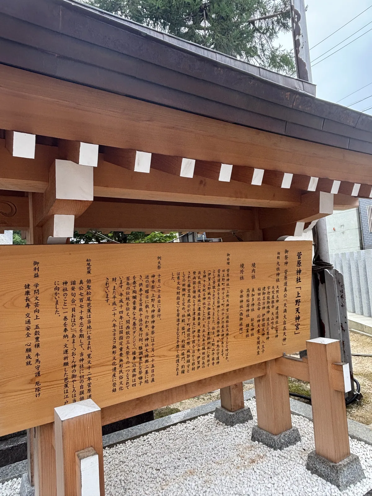 木造屋頂的大立牌。右欄記御祭神菅原道真公與相殿九社神社的十二位神名；來歷那一欄寫「往古、上野山平楽寺（伊賀上野城内）の伽藍神として農耕神祇に発祥する神々を祀る神社でした」——很久以前，這裡是上野山平樂寺的伽藍神，祀的是從農耕神祇發源的神們；並記天正九年織田信長的兵亂後遷座、慶長十三年藤堂高虎定為城郭鎮守的祈願所。左端另有松尾芭蕉與御利益兩欄。