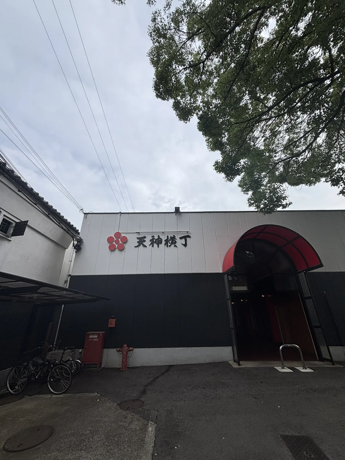 神社西鄰的建物，上白下黑，正面掛紅色的梅鉢紋與店名，入口是一道紅色的拱。