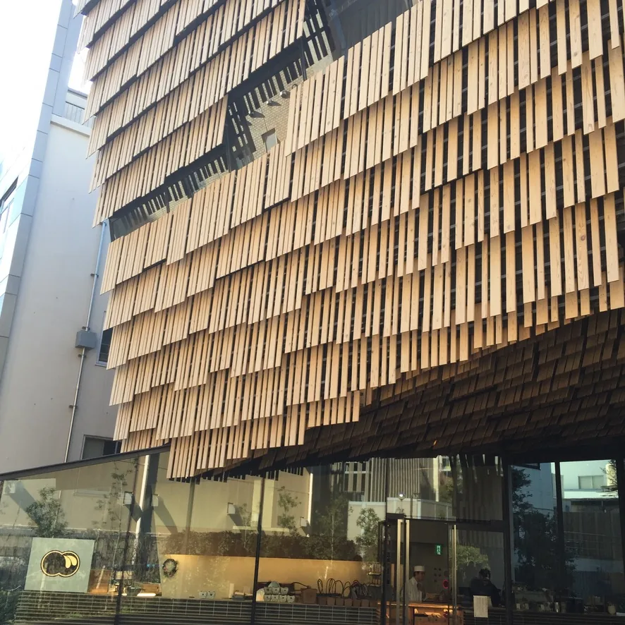 自校內小巷北望研究館，杉板外裝沿著小巷連續展開，左側是鄰棟的白色校舍，小巷上有行人