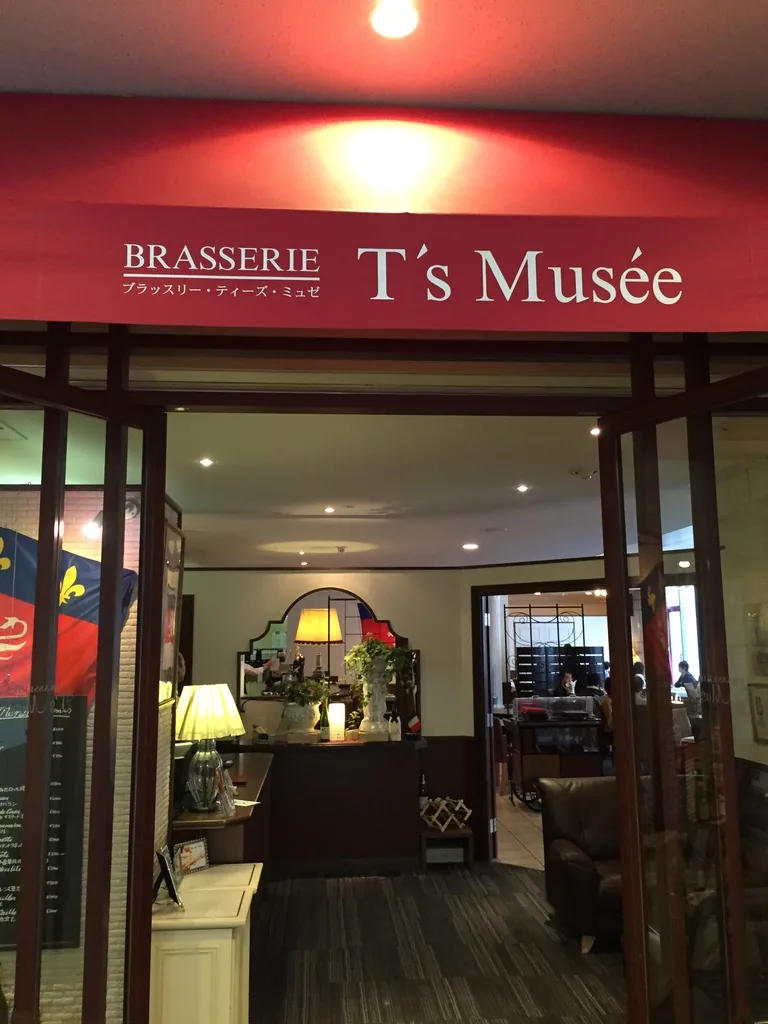 館內餐廳 Brasserie T's Musée 的店口，紅色的招牌上寫著店名，入口內是以深色木框、檯燈與皮革沙發裝修的室內