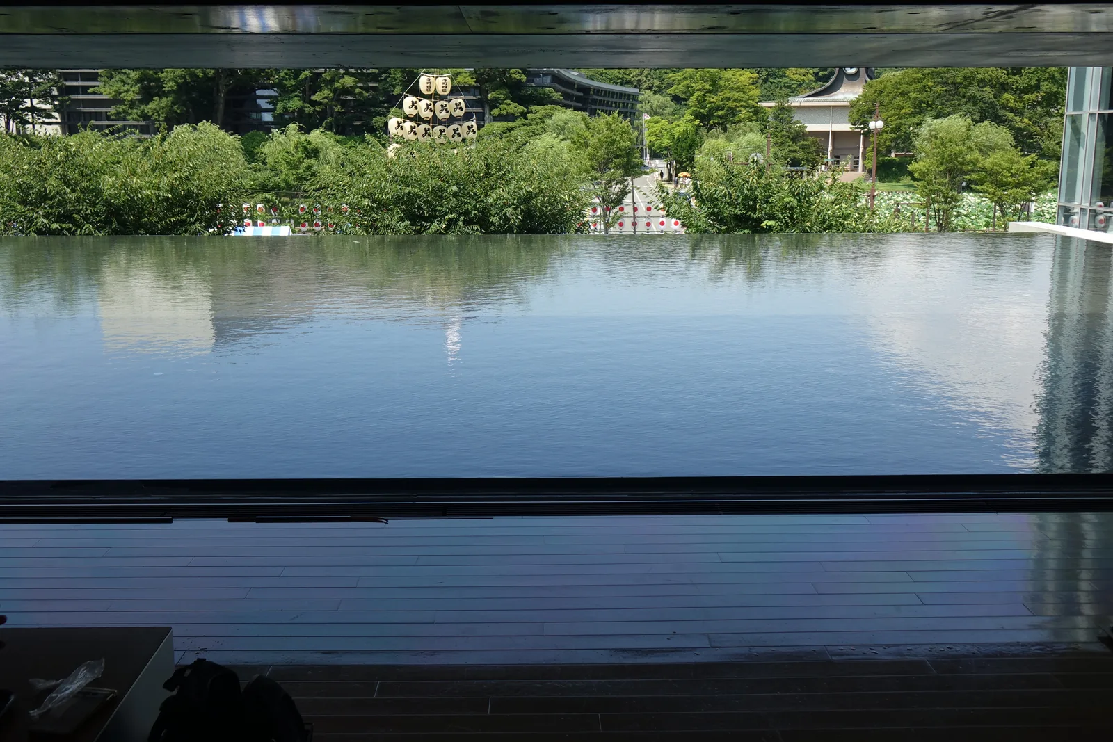 自二樓 lounge 望向水庭，水面與窗台齊平，對岸的柳樹叢中立著一支竿燈，樹後可見一座屋頂兩端上揚的白色建築