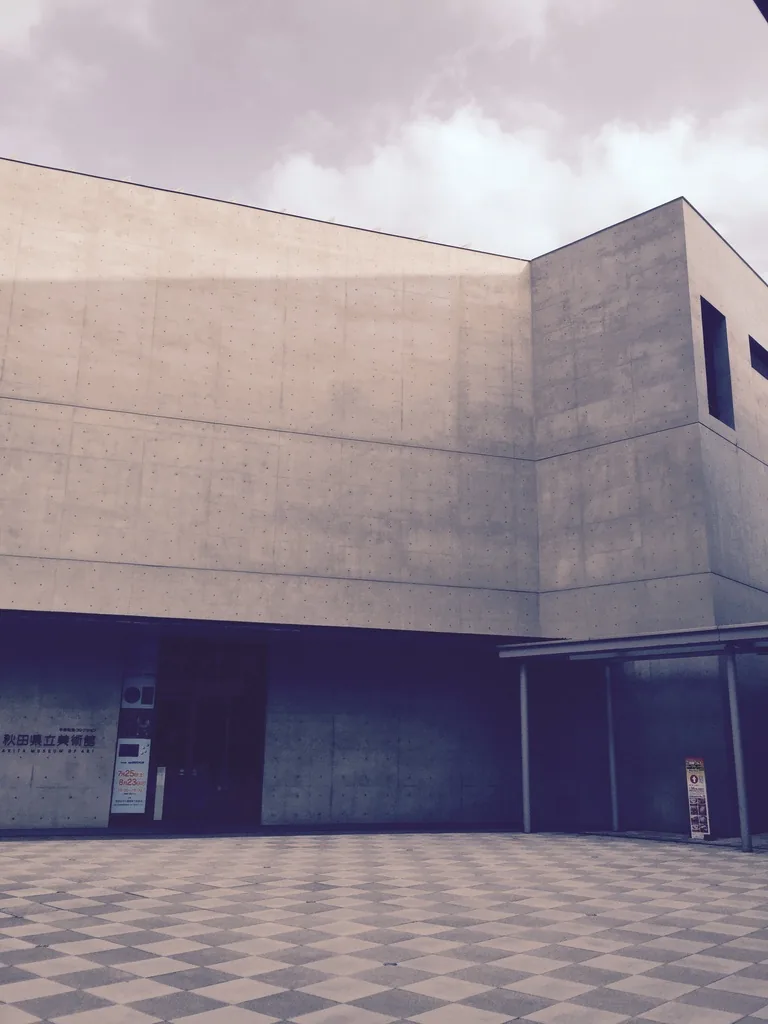 美術館東南角，上層量體的轉角向外出挑，下層後退處設有入口與館名，地面為黑白相間的格紋鋪面
