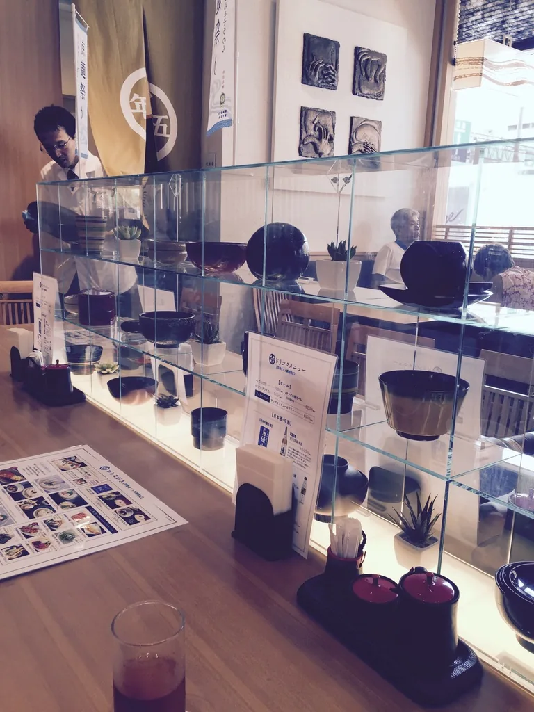 寬文五年堂店內，木製吧台上方是多層玻璃展示櫃，陳列著漆碗與漆器，後方牆上掛著店的紋樣