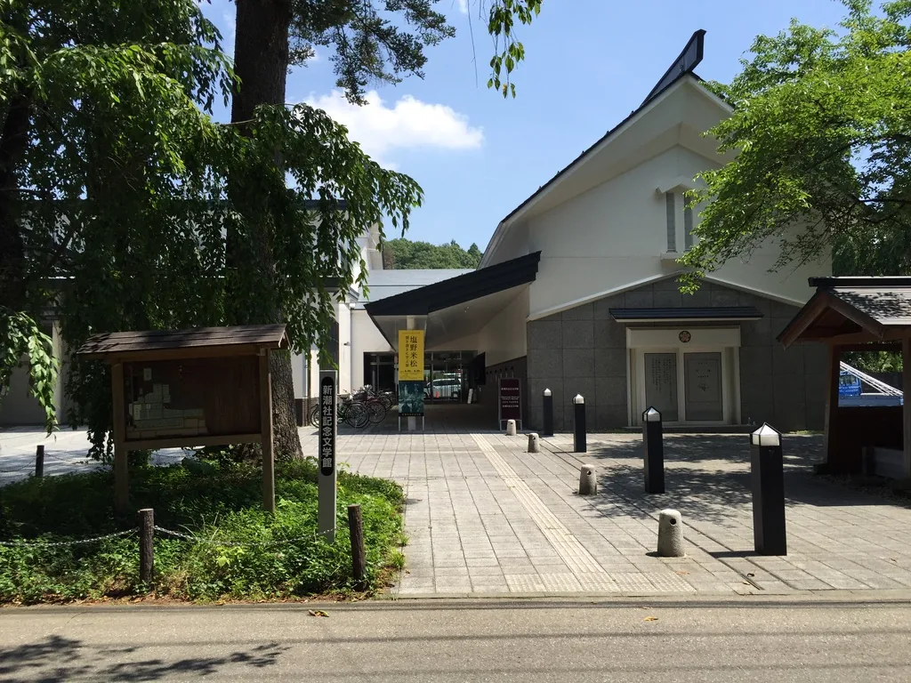 新潮社記念文學館與仙北市總合情報中心的正面，白色灰泥的上層牆面頂著一道不對稱的陡坡屋頂，下層為灰色石材，前方是鋪石的前庭與成列的車擋，左側立著木製的告示板