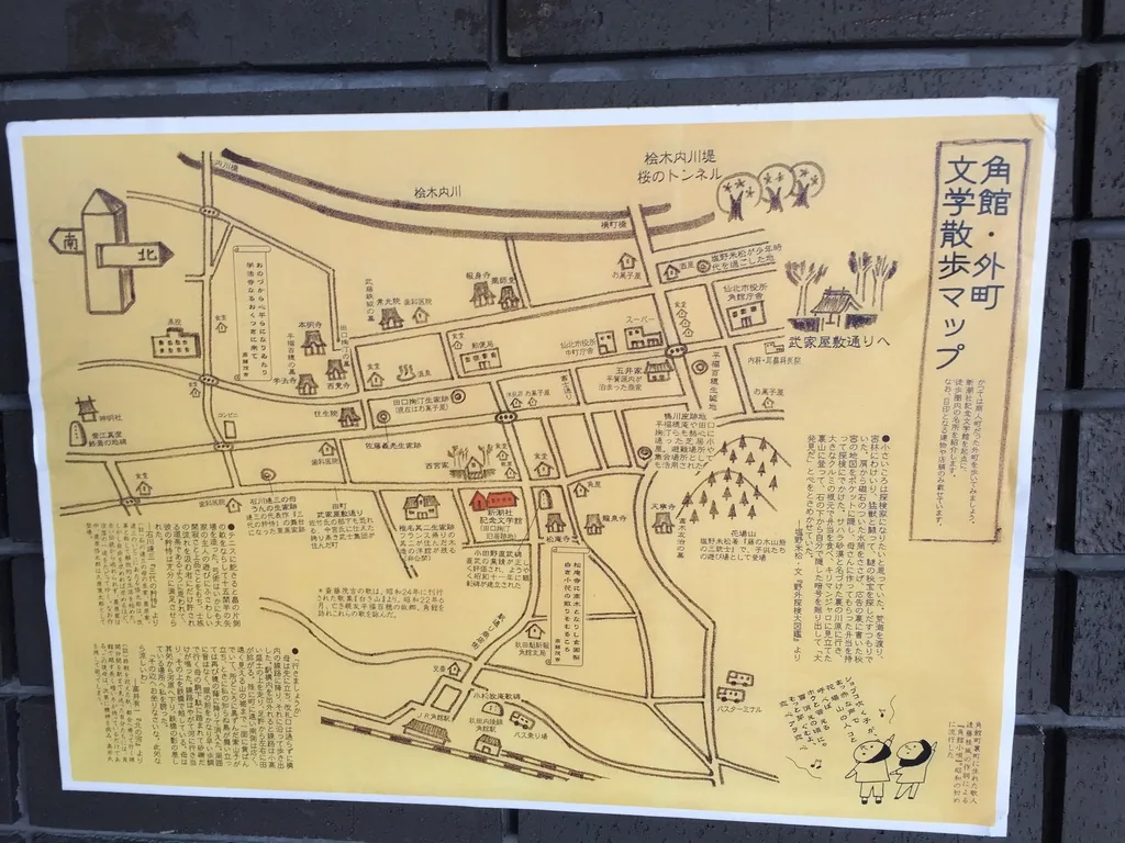 深色磚牆上貼著一張手繪的角館外町文學散步地圖，地圖以黑線繪出街道與地點，周邊以小字寫著說明，右下角畫著兩個人物