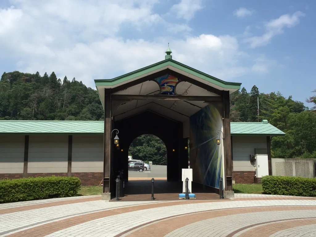 自園內回望銀河車站：深綠色屋頂的山牆門樓，通路兩側牆面繪有放射狀光芒，遠處可見停車場