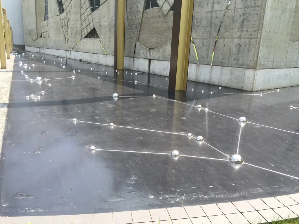 黑色地坪上以金屬細線與銀色圓球連成星座，後方是金色鋼框與混凝土牆