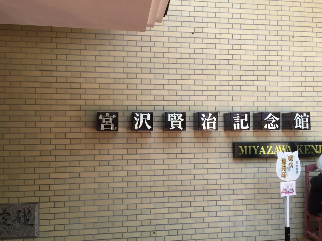 淺黃色磚紋牆面上，以黑底白字的立體方塊拼出館名，下方是英文館名的銘板，左下角嵌著定礎石，上方可見玄關的簷