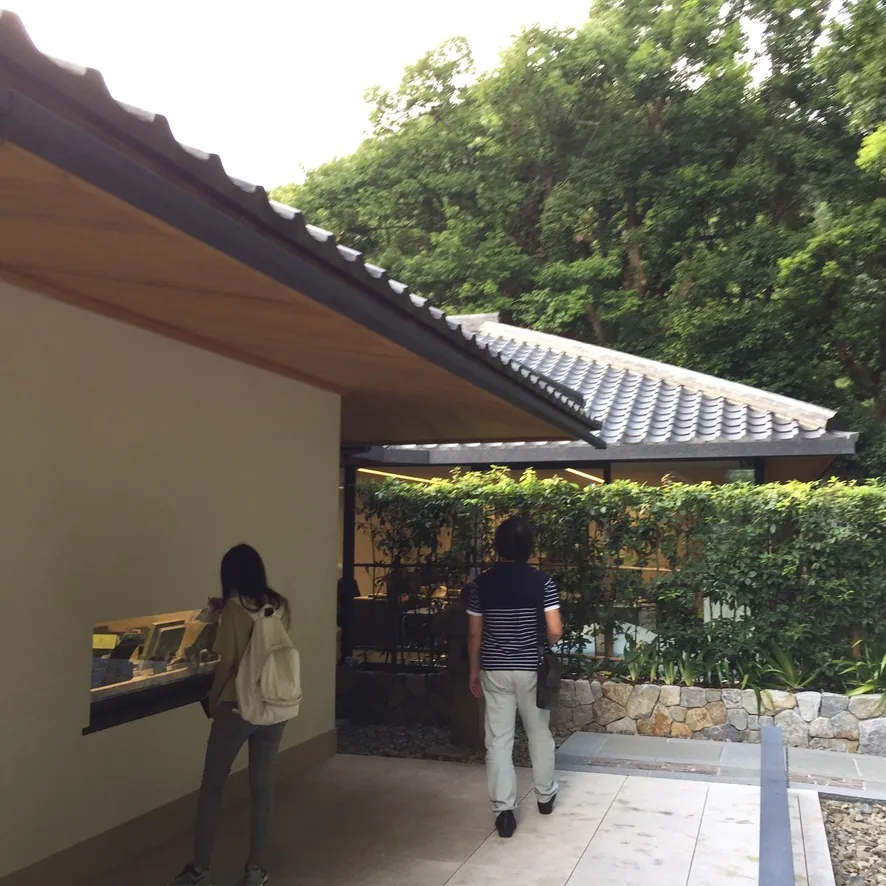 館舍之間的中庭，左側是一道以白色漆喰塗成的牆與瓦葺的屋頂，屋頂下方是一扇小型的展示窗，右側是另一棟瓦屋頂的建築與石砌的牆基，綠籬與樹木圍在中庭四周，兩位參觀者站在牆前