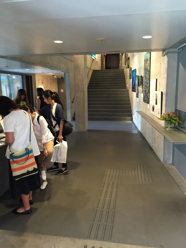 入口大廳的內部，左側是混凝土的服務台，正面一道直跑樓梯沿著清水混凝土牆向上延伸，牆上掛著數幅攝影作品，天花是白色平頂與嵌燈，地面鋪著灰色地坪與導盲磚