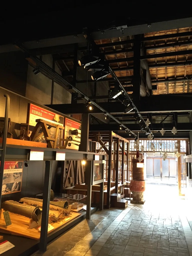 石板鋪面的通道向深處延伸，左側是兩層鋼架展示框與紅色說明板，上方露出既存的木屋架與屋面板，屋面上開有天窗，通道盡頭是明亮的開口