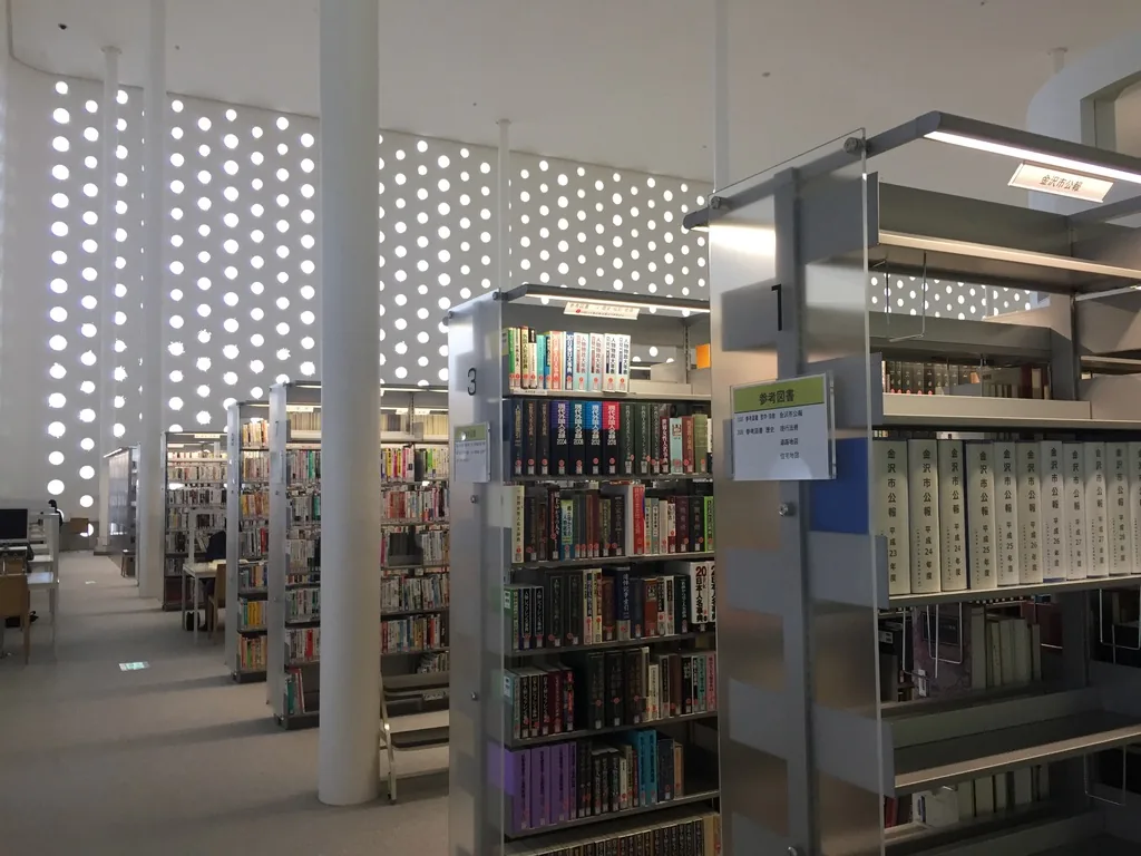 二樓一般圖書區，前景是兩座高書架，書架之間立著白色細圓柱，遠處的外牆整面布滿發光的圓孔，閱讀桌與書架混合排列