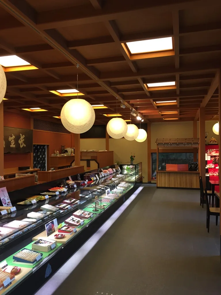 一樓店舖的內部，天花是木製的格天井，格間嵌有方形燈箱，下方懸掛一列白色球形燈，左側是長排的玻璃展示櫃，牆上掛著題字匾額