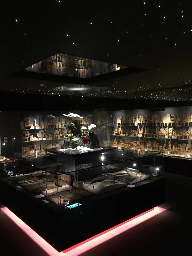 展示室的全景，深色的天花上散布細小的光點，中央是一座下緣發出紅光的低矮展示台，台上有花材與展示物，四周牆面排滿木型
