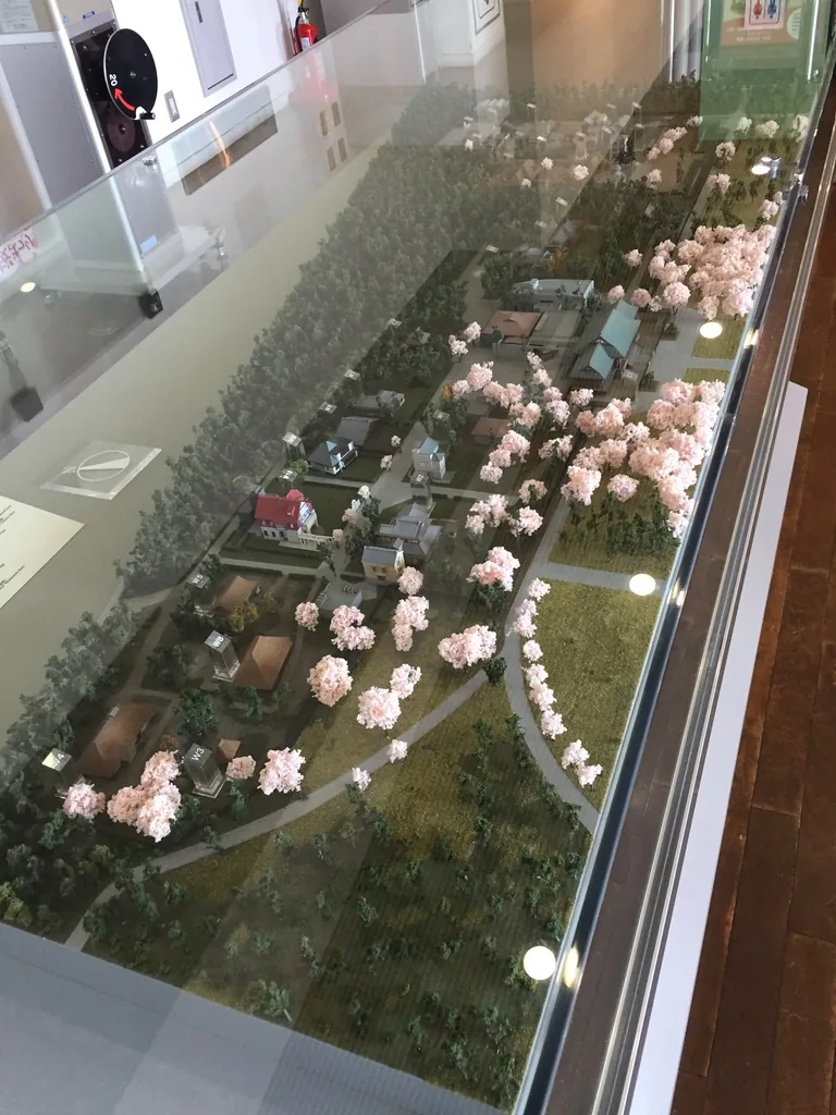 遊客中心內的全園模型，玻璃展示櫃中是縮尺的園區，綠色的樹林間散布著屋頂與開花的櫻樹，展示櫃旁是白色的牆面