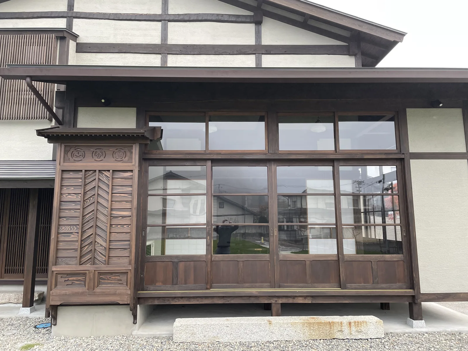 建築側面，木造的一樓外牆嵌有木框玻璃窗與格子門，上方為深簷，背景為霧中的山