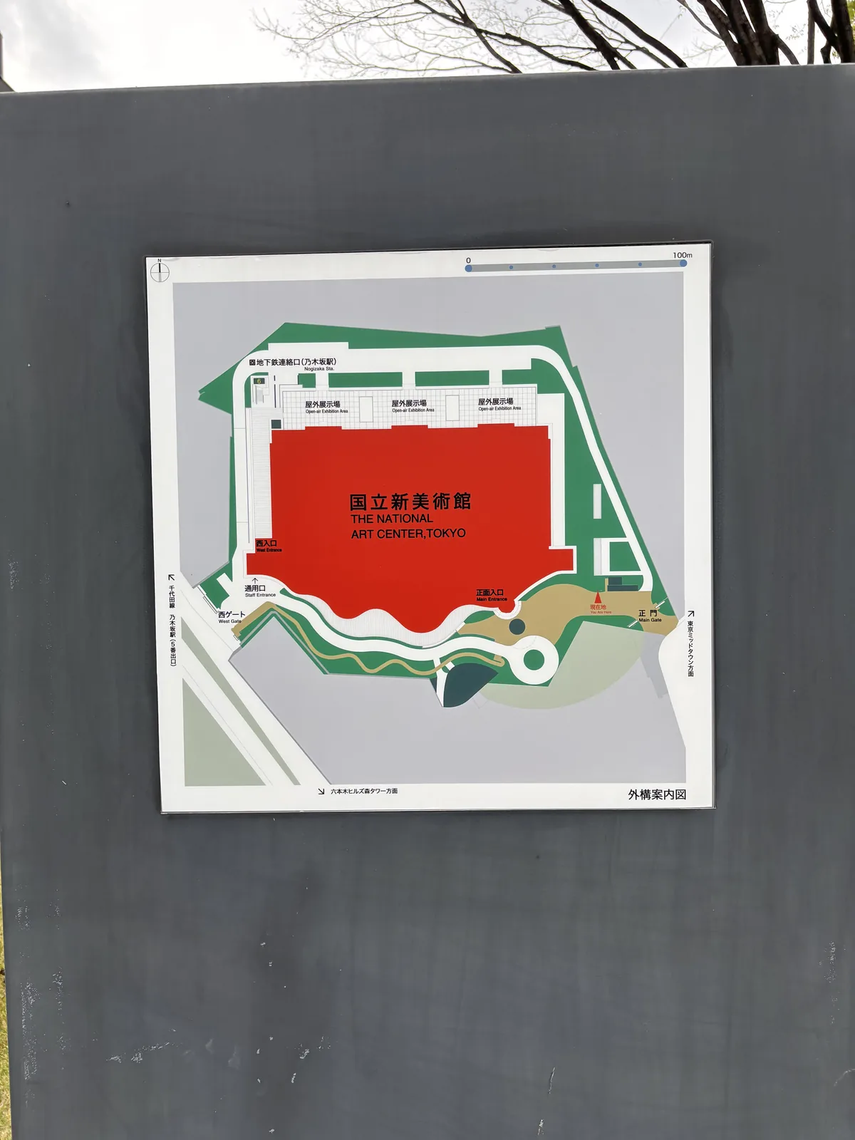 外構案內圖的看板，以紅色塊標示美術館本體，周圍以綠色標示植栽，南側沿著建築畫出波浪狀的輪廓，北側標有野外展示場
