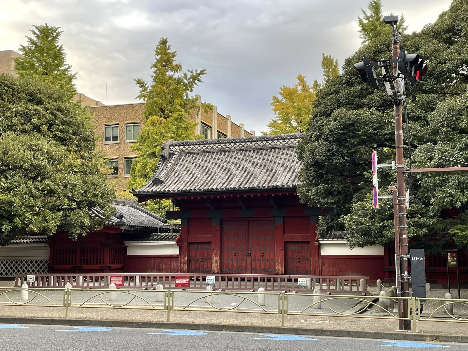 本鄉通旁的赤門，朱紅色的門體上覆著本瓦葺的切妻屋頂，左右兩側是唐破風屋頂的番所與白色的海鼠牆，門扉緊閉，前方是人行道的護欄與道路