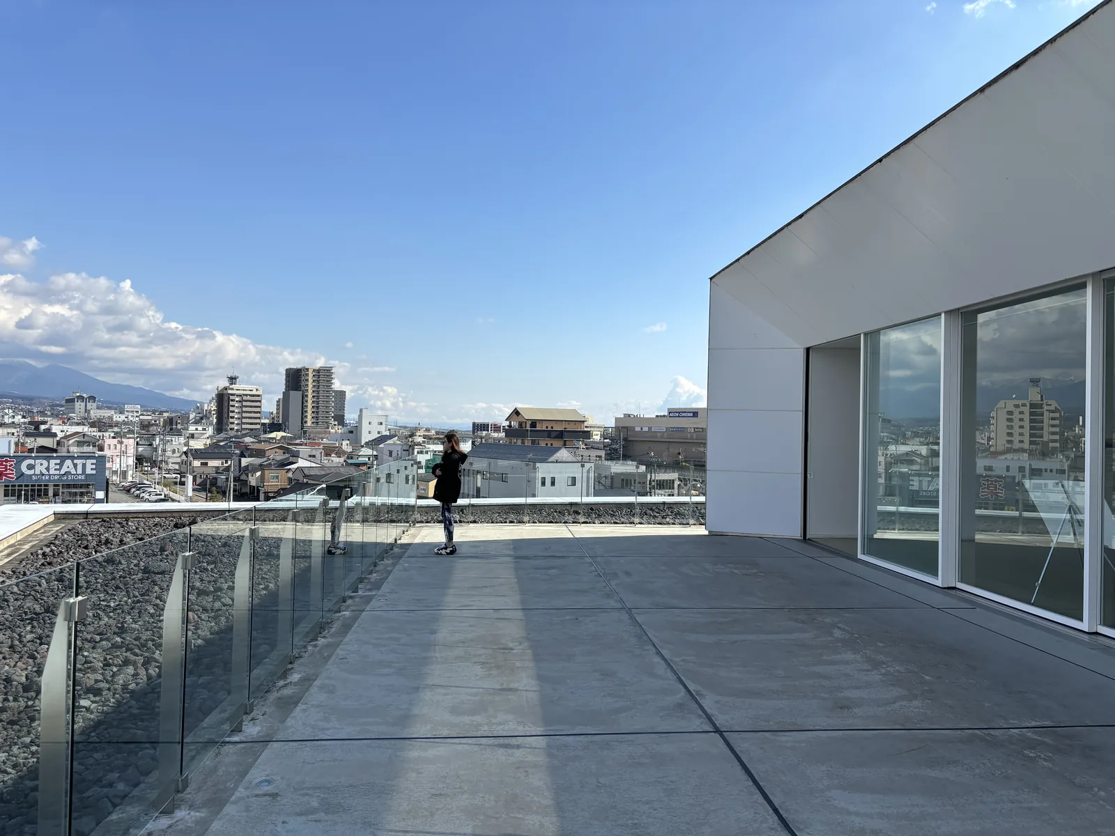 屋外露台，右側是展望廳的白色外牆與玻璃開口，地面為石板，玻璃欄杆外鋪著深色碎石，遠方是市街