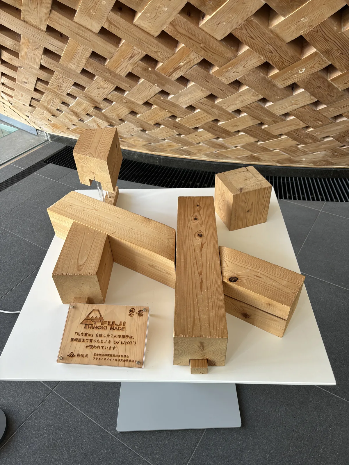 白色展示台上放著數段相互搭接的方形檜木構材樣品，構材上刻有搭接用的缺口，後方是木格子的斜面