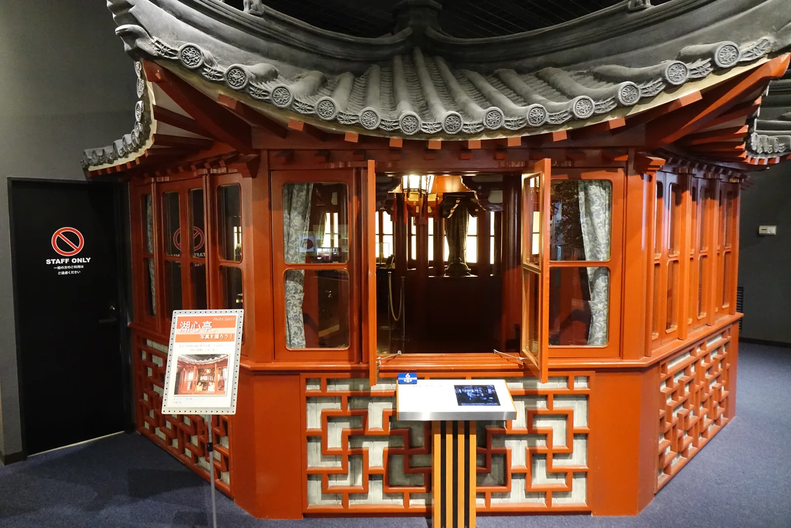 展示室內的中國茶館再現，紅漆的木構與格子欄杆，灰瓦的屋頂簷角起翹，內部可見木桌椅與吊燈