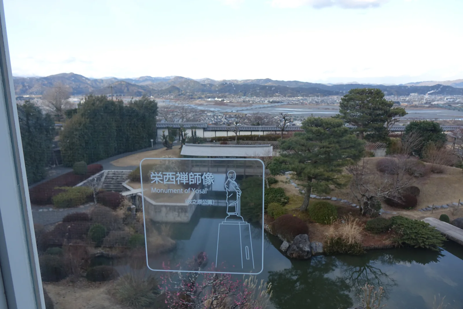 落地窗外是有水池與松樹的庭園，遠方是河谷、市街與山，玻璃上印著白色線描的立像與「榮西禪師像」的中英文標示