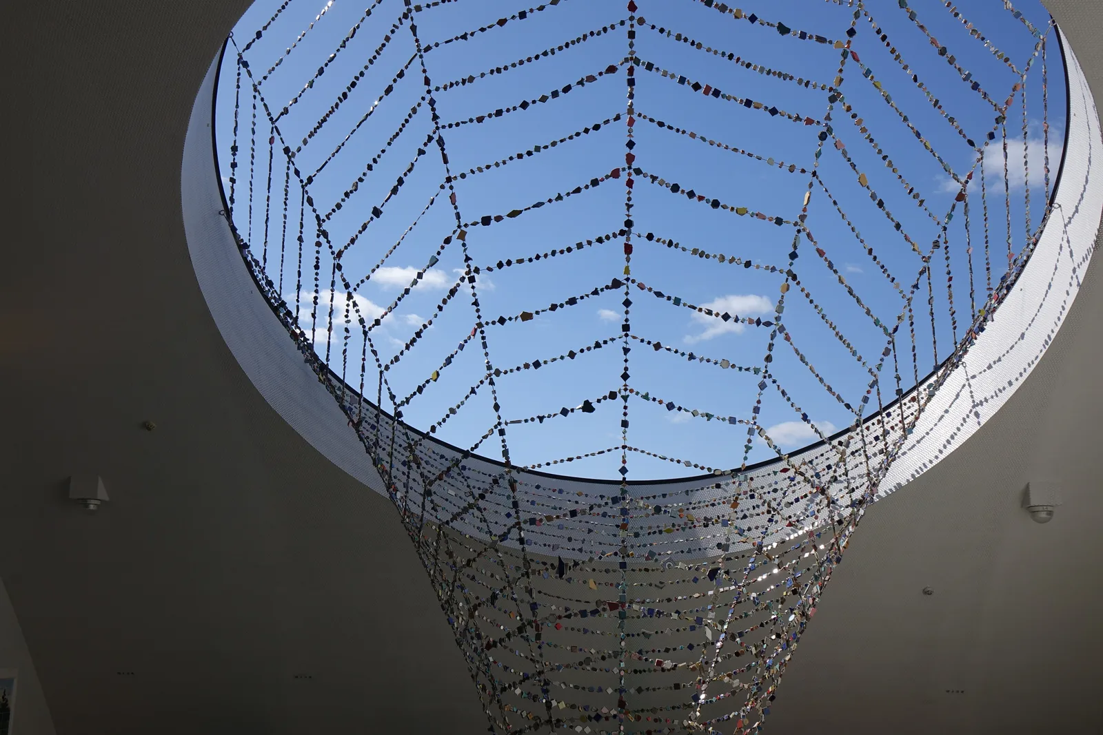 自下方仰望屋頂的圓形開口，藍天之前是以鋼索編成的漏斗狀網，鋼索上綴滿各色的磁磚碎片