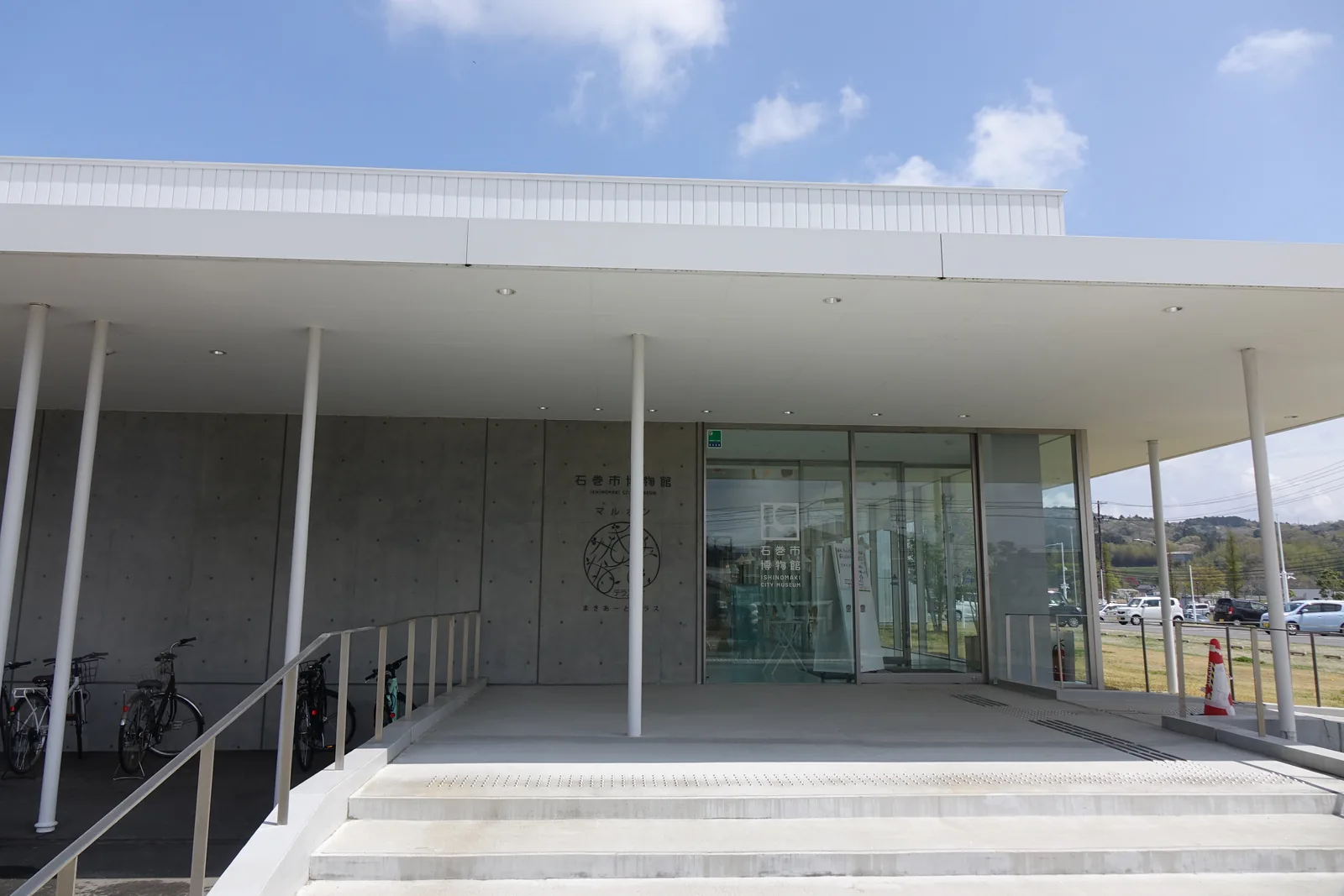 石巻市博物館側門：留有模板痕跡的灰色混凝土牆面與「Maruhon」圓形標誌